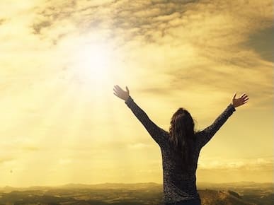 A picture of a person who has open arms to a bright sun.