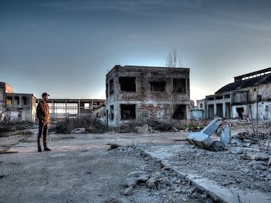 A picture of a man standing outside abandoned buildings.